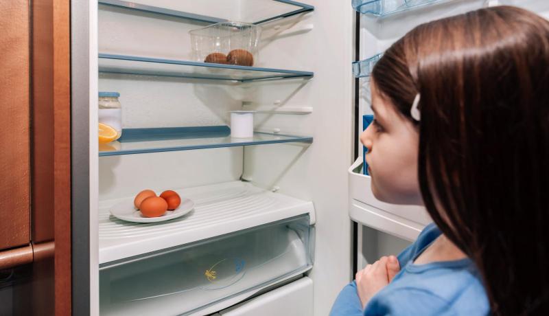 ein Mädchen steht vor einem leeren Kühlschrank
