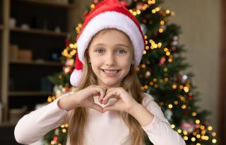 Mädchen formt mit beiden Händen ein Herz vor dem Weihnachtsbaum
